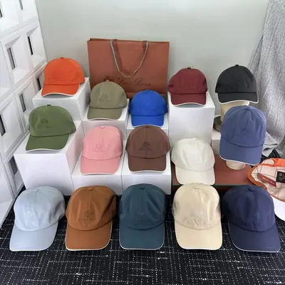 Twelve baseball caps in orange, olive, brown, navy, pink and pale blue, displayed on white blocks