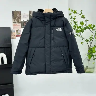 A black hooded puffer jacket hanging on a rail beside a cardboard box and a houseplant